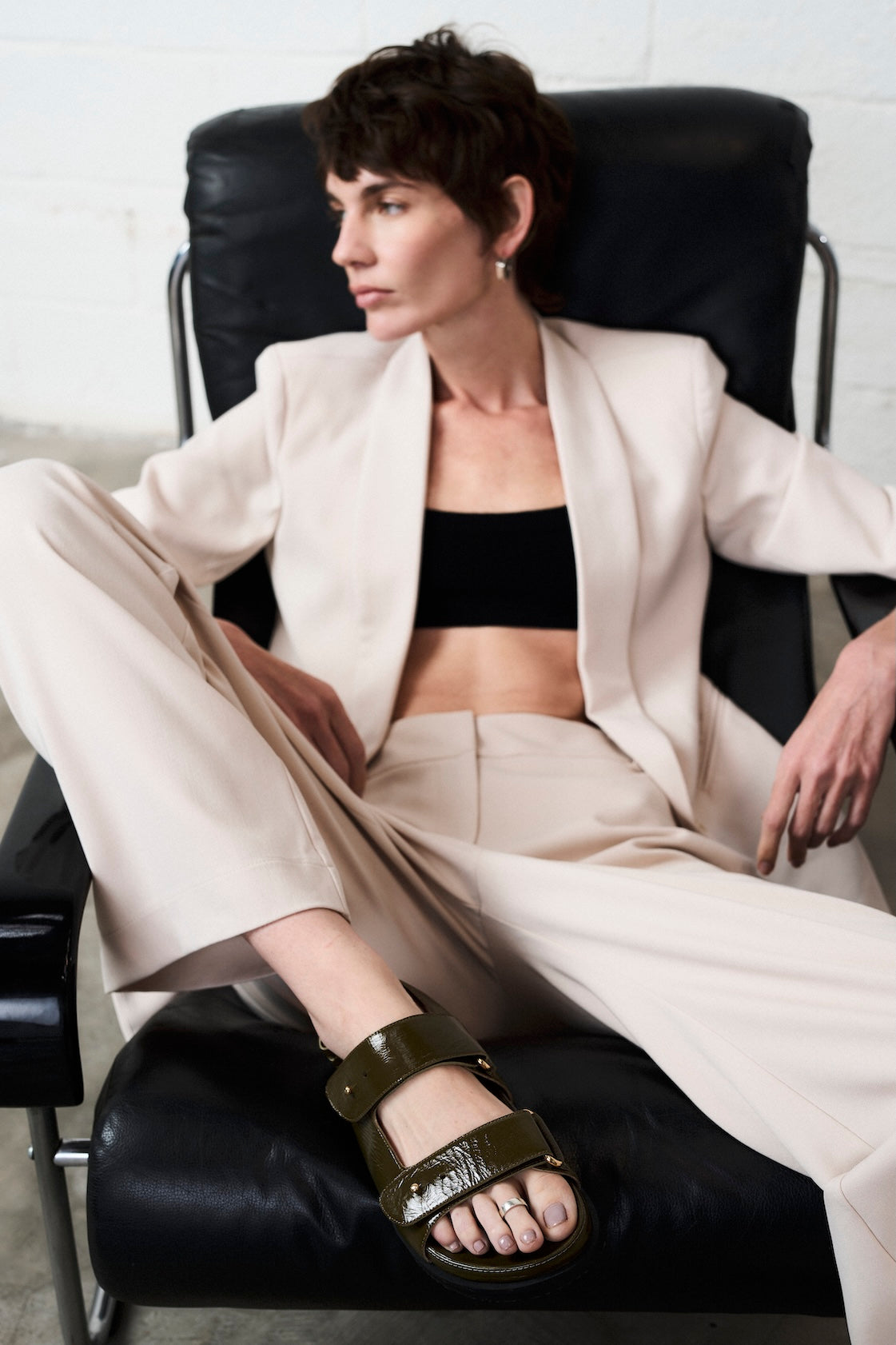 Woman in a beige suit sitting in a chair wearing Margot Green Leather Chunky Sandals by Mafalda Handmade
